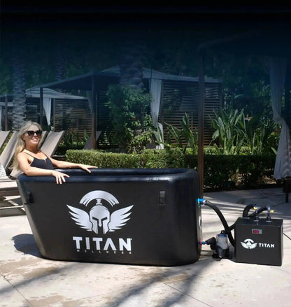 “Triumph XL cold plunge in black connected to the Titan water chiller, shown in use outdoors with a woman relaxing in the tub on a sunny patio.”