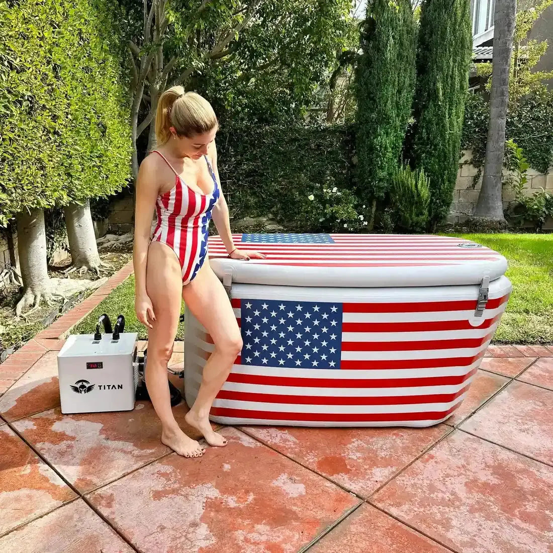 Person in a patriotic swimsuit standing next to an inflatable hot tub with American flag design.